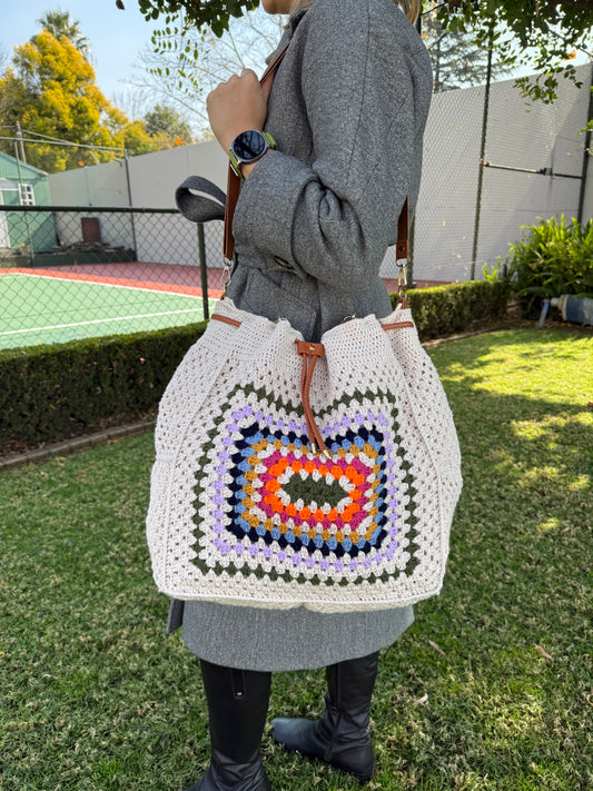 Close up of a cream crochet granny square bag showing colorful textured stitches, drawstring closure and leather details.