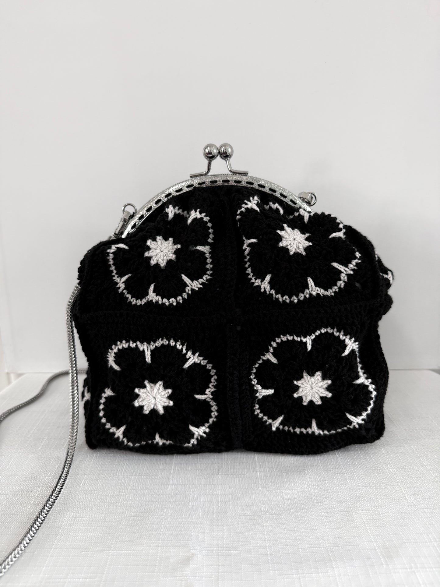 Black handmade crochet kiss lock handbag with white floral granny square design and silver chain strap
