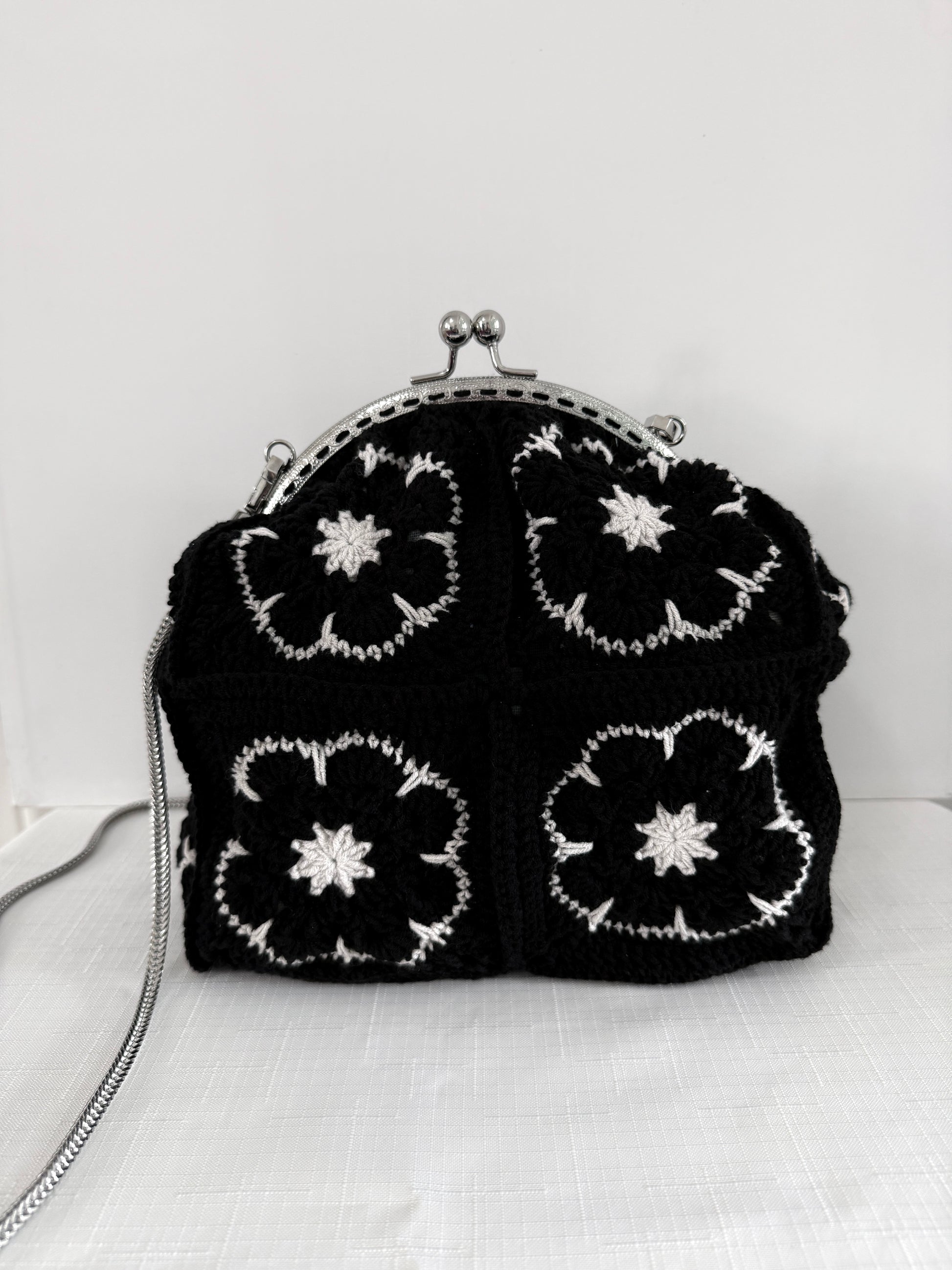 Black handmade crochet kiss lock handbag with white floral granny square design and silver chain strap