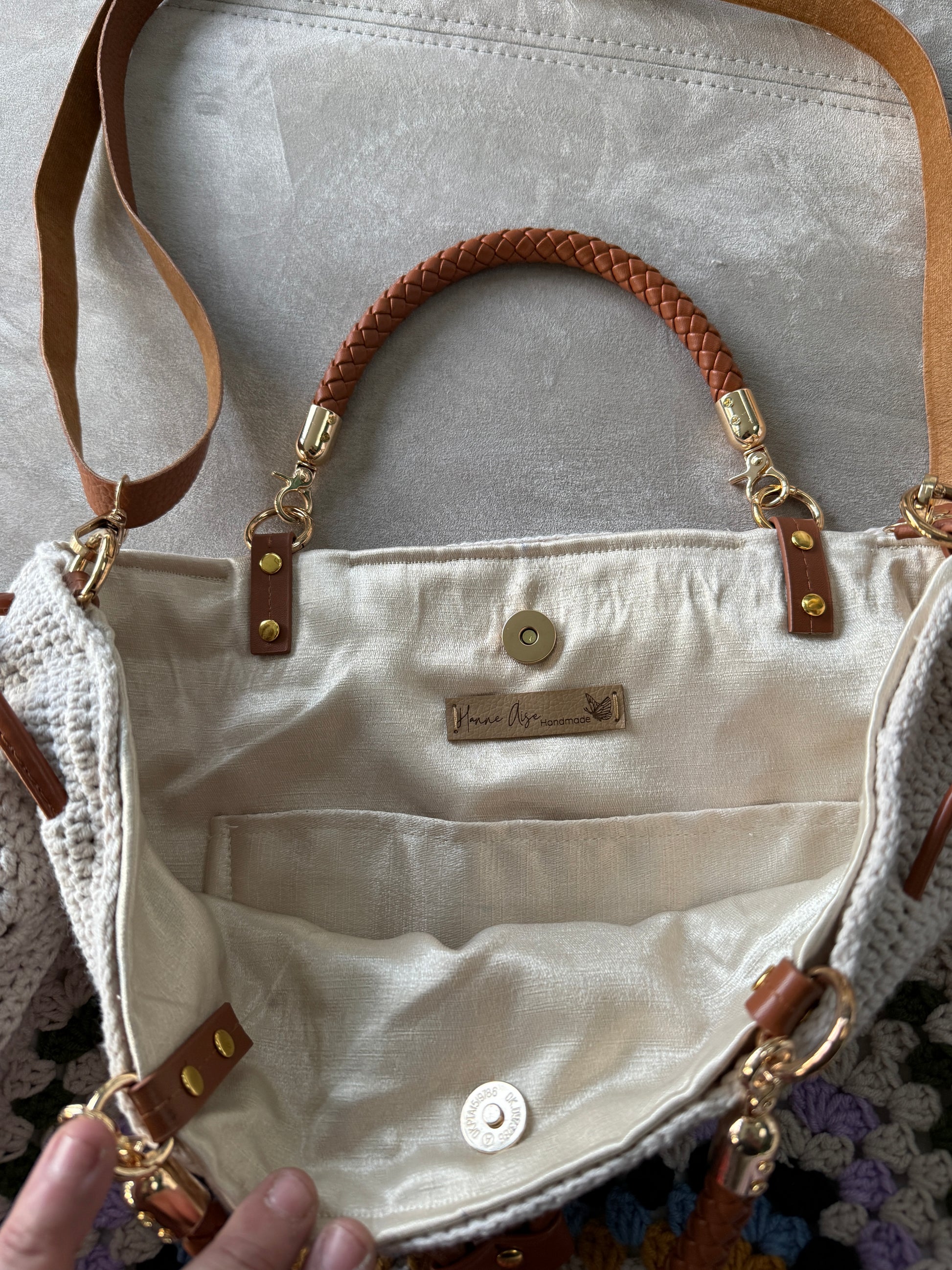 Close up of a cream crochet granny square bag showing colorful textured stitches, drawstring closure and leather details.
