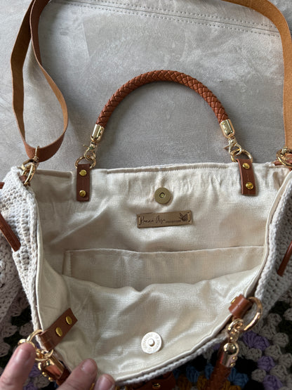 Close up of a cream crochet granny square bag showing colorful textured stitches, drawstring closure and leather details.
