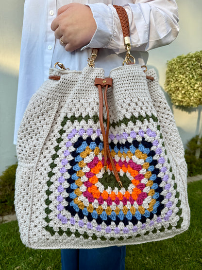 Person holding a colorful crochet bag with a geometric pattern outdoors.