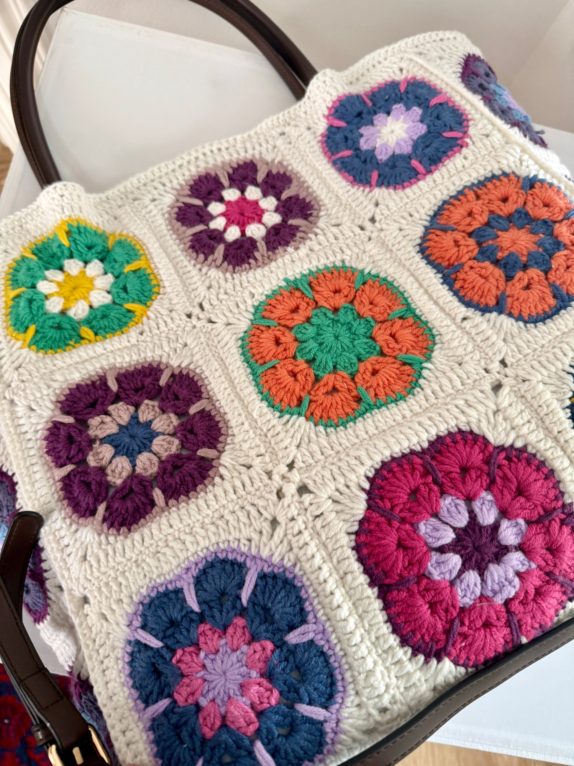 Close up of handmade floral granny square crochet tote bag with textured cream stitches