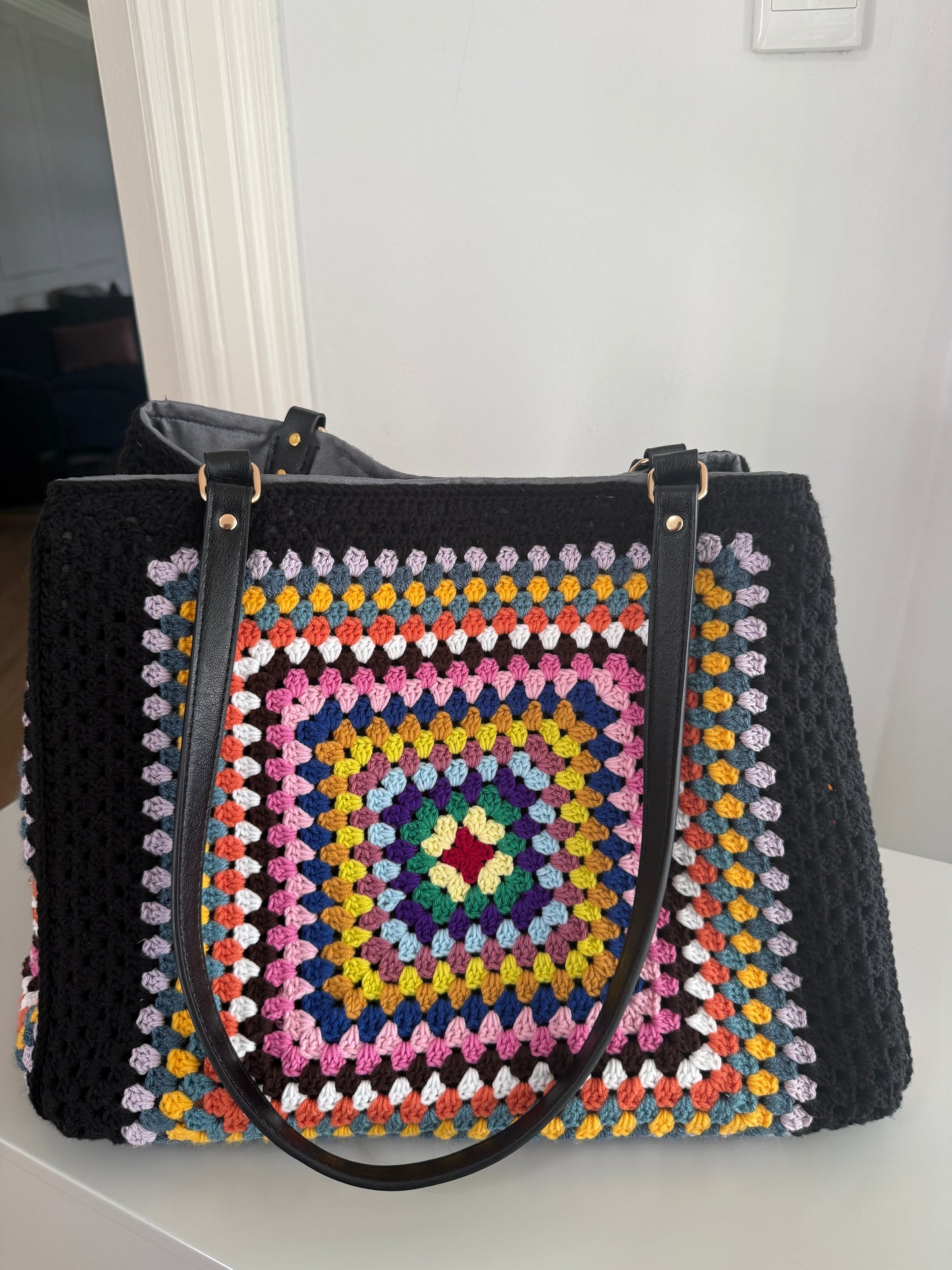 Black handbag with a colorful crochet pattern on a white surface.