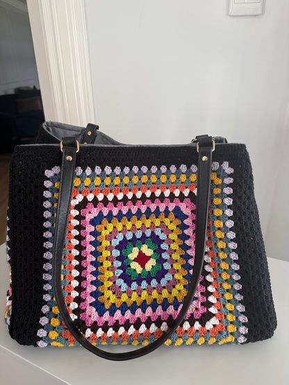 Black handbag with a colorful crochet pattern on a white surface.