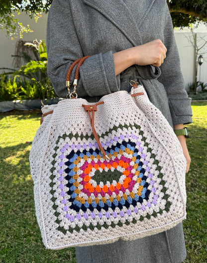 Large handmade crochet drawstring bag with colorful granny square front panel, leather straps and braided top handle.
