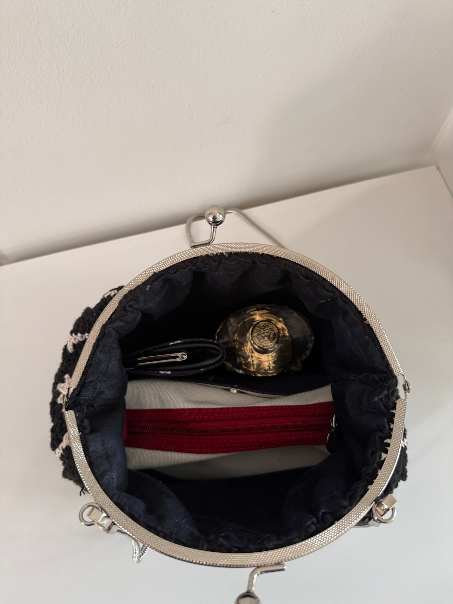 Black crochet kiss lock handbag open to show lined interior and everyday evening essentials
