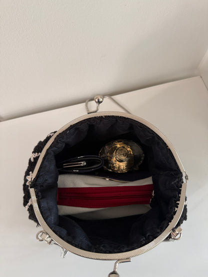 Black crochet kiss lock handbag open to show lined interior and everyday evening essentials