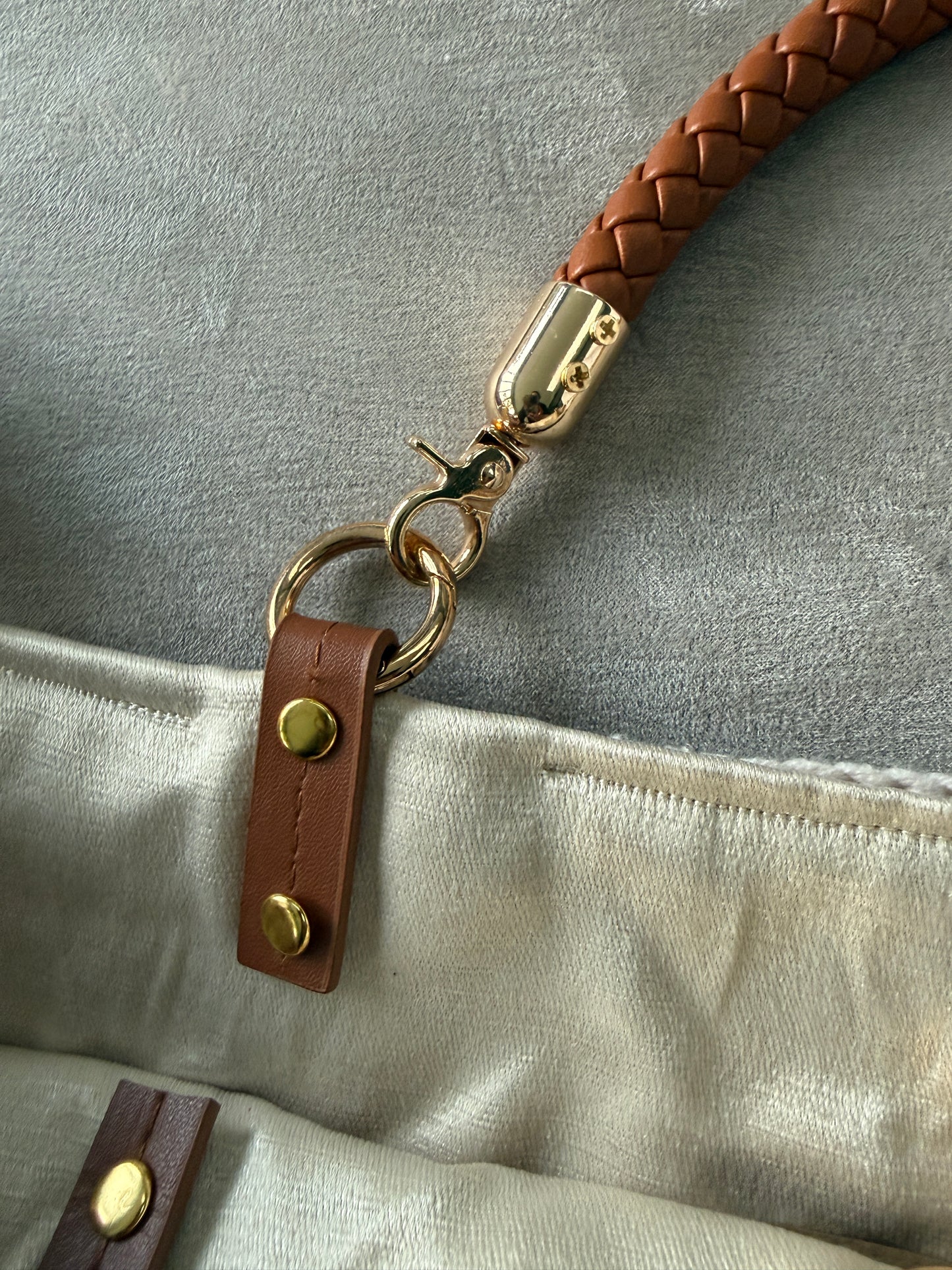 Close-up of a braided leather strap with gold hardware attached to a beige fabric surface.