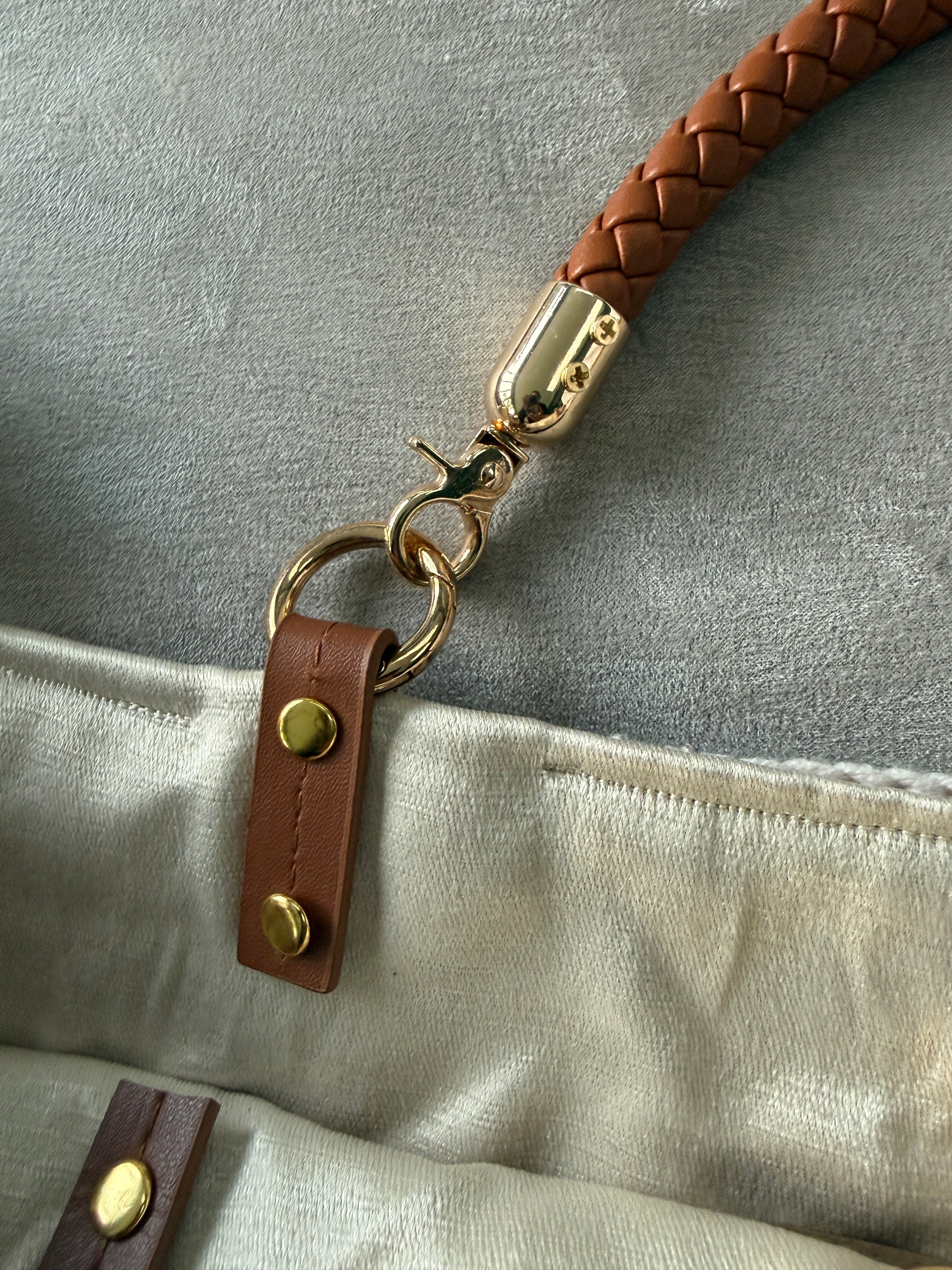 Close-up of a braided leather strap with gold hardware attached to a beige fabric surface.