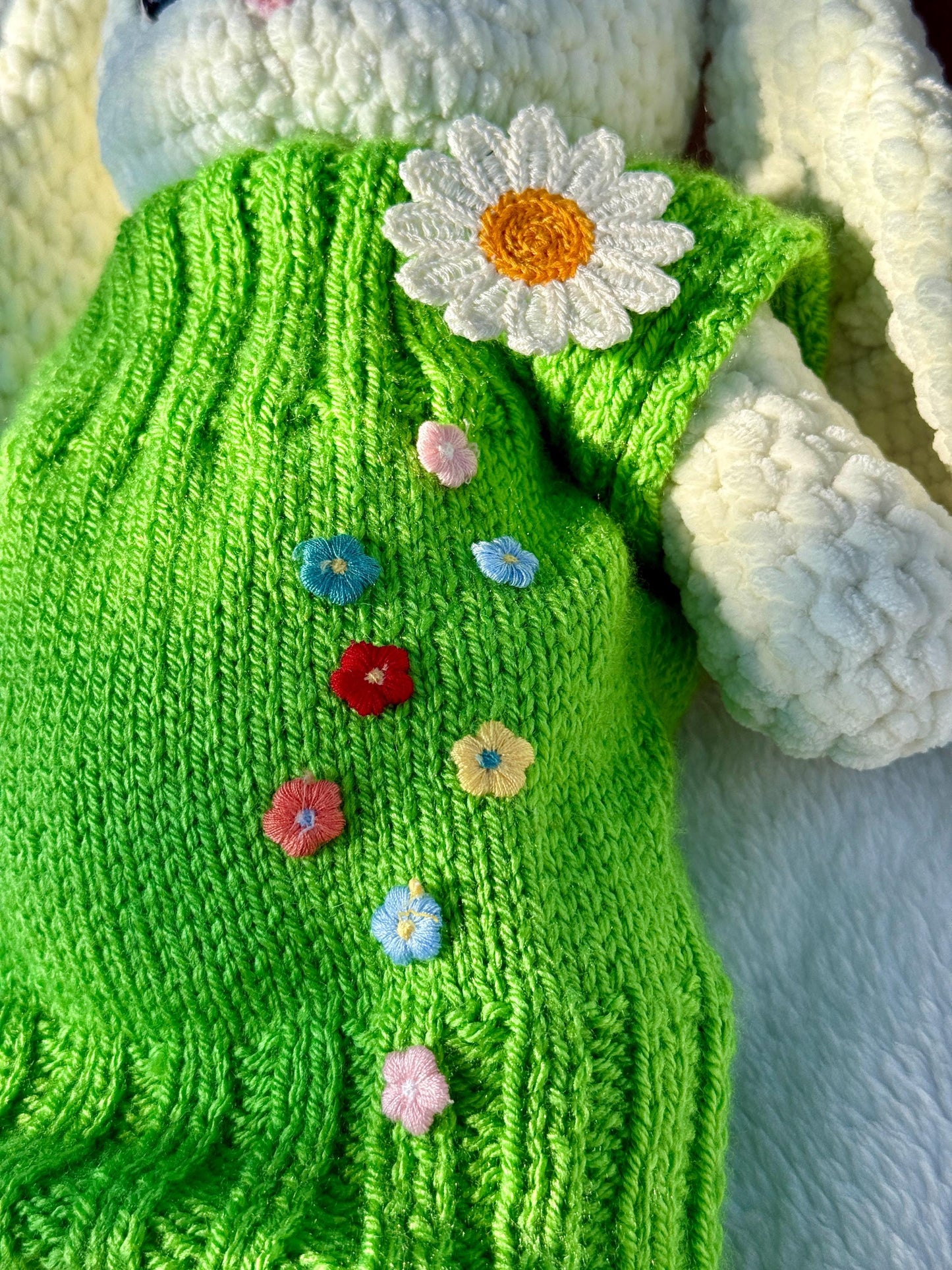 Close-up of handmade crochet bunny in green dress with embroidered colorful flowers and a white daisy.