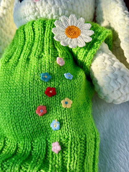 Close-up of handmade crochet bunny in green dress with embroidered colorful flowers and a white daisy.