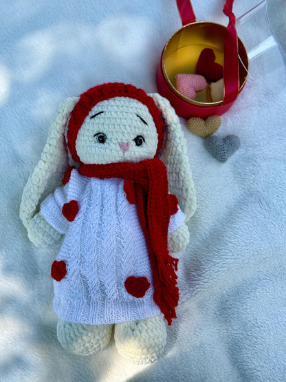 Crochet bunny doll with red knitted scarf and white dress decorated with red hearts.