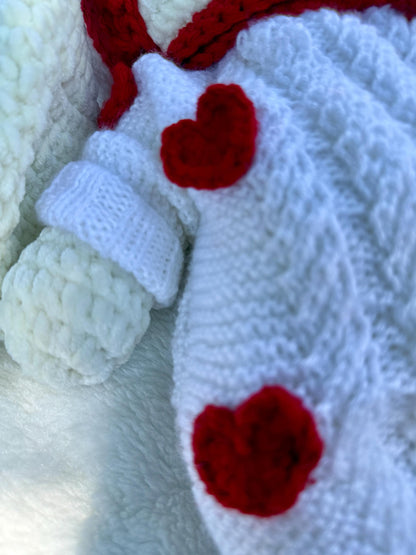 Macro shot showing red heart crochet applique detail on bunny’s knitted white dress.