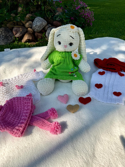 Crochet bunny surrounded by multiple handmade outfit sets in pink, red, and green.