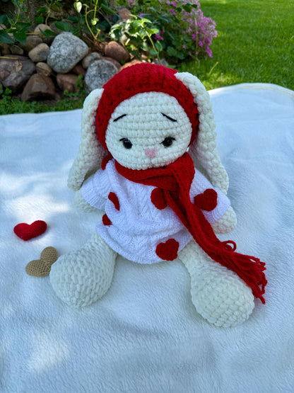 Handmade bunny doll in red heart dress and hat sitting on a soft blanket with hearts beside it.