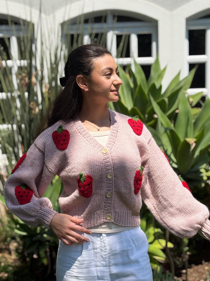 Handmade strawberry crochet cardigan in soft blush pink, modeled outdoors.