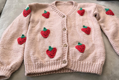 Flat lay of strawberry cardigan with cotton appliqués, ready for packaging.